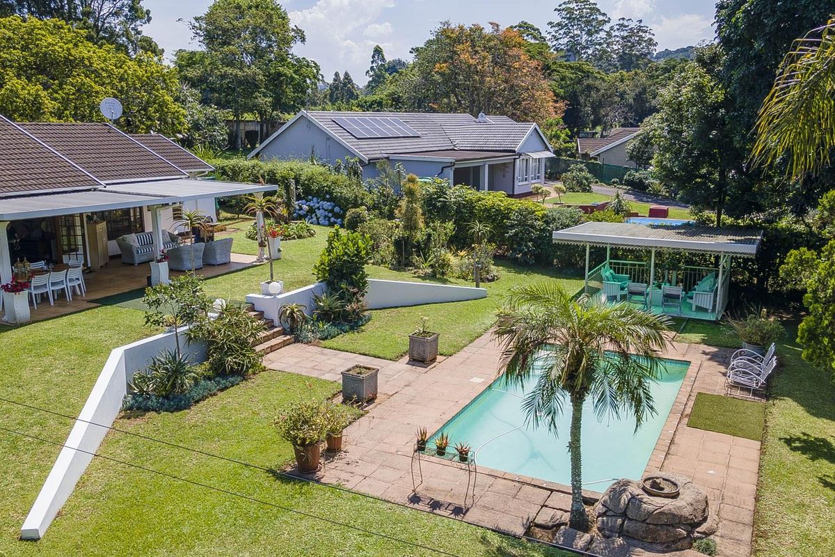 Aerial view of a spacious residential property featuring a landscaped garden, swimming pool, covered patio, and a detached gazebo in a lush setting.