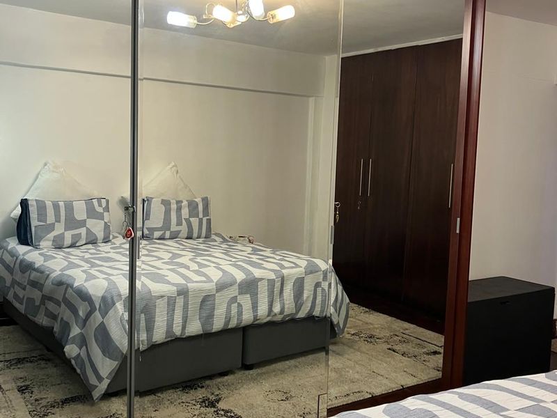 Spacious bedroom featuring parquet flooring, a large built-in mirrored sliding wardrobe, and additional dark wood cabinetry for ample storage.