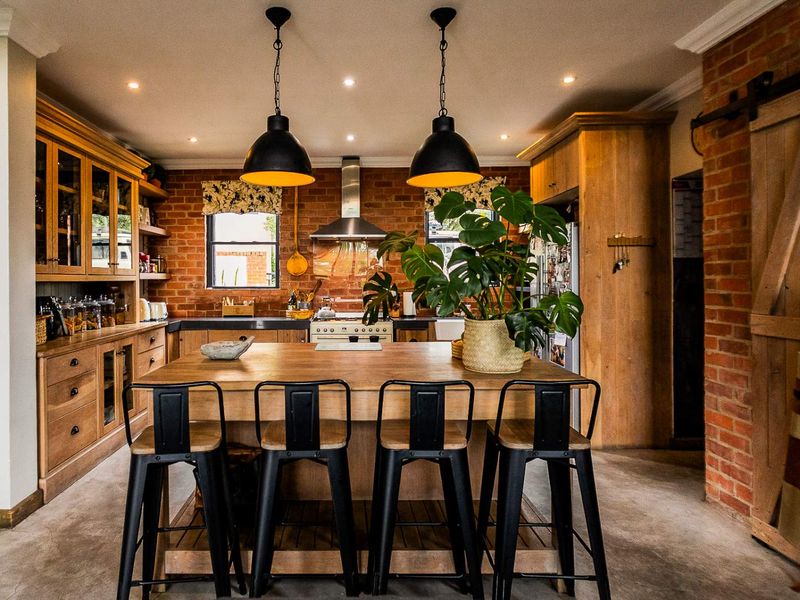 A rustic-style kitchen featuring exposed brick walls, custom wooden cabinetry, a central island, and modern industrial pendant lighting.