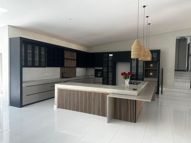 Modern kitchen featuring sleek black cabinetry, concrete countertops, a large central island with slatted timber accents, and high-end integrated appliances.