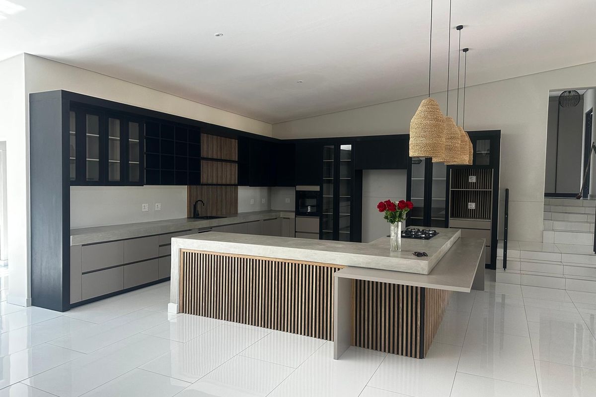 Modern kitchen featuring sleek black cabinetry, concrete countertops, a large central island with slatted timber accents, and high-end integrated appliances.