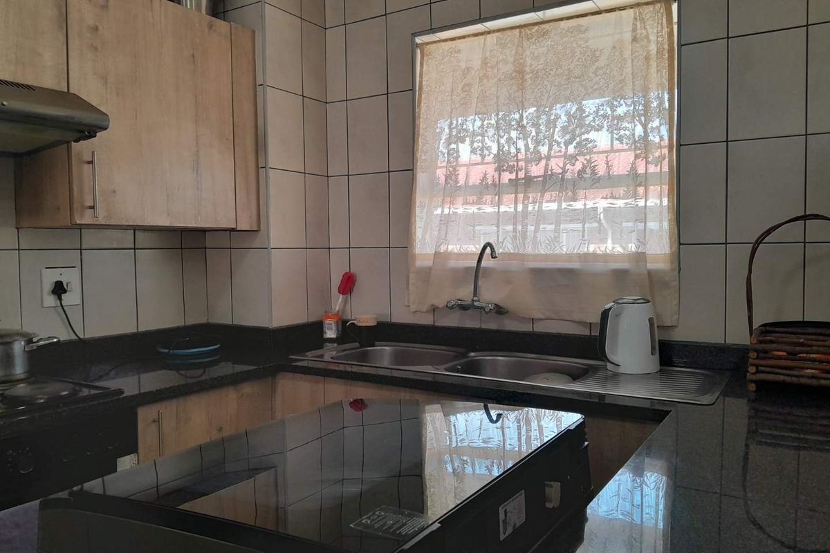 A functional kitchen featuring granite countertops, a double bowl stainless steel sink, tiled splashbacks, and built-in wooden cabinetry.