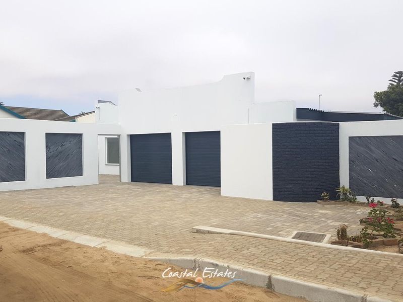 Modern front facade featuring a double garage with roller shutter doors, paved driveway, and decorative stone cladding accents.