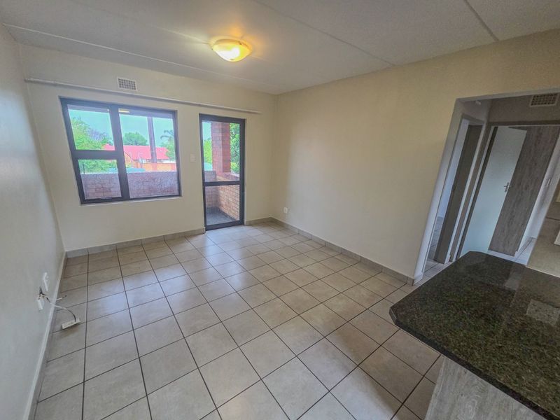 An empty open-plan living area featuring neutral tiled flooring, a granite breakfast bar, and direct access to a balcony through an aluminium door.