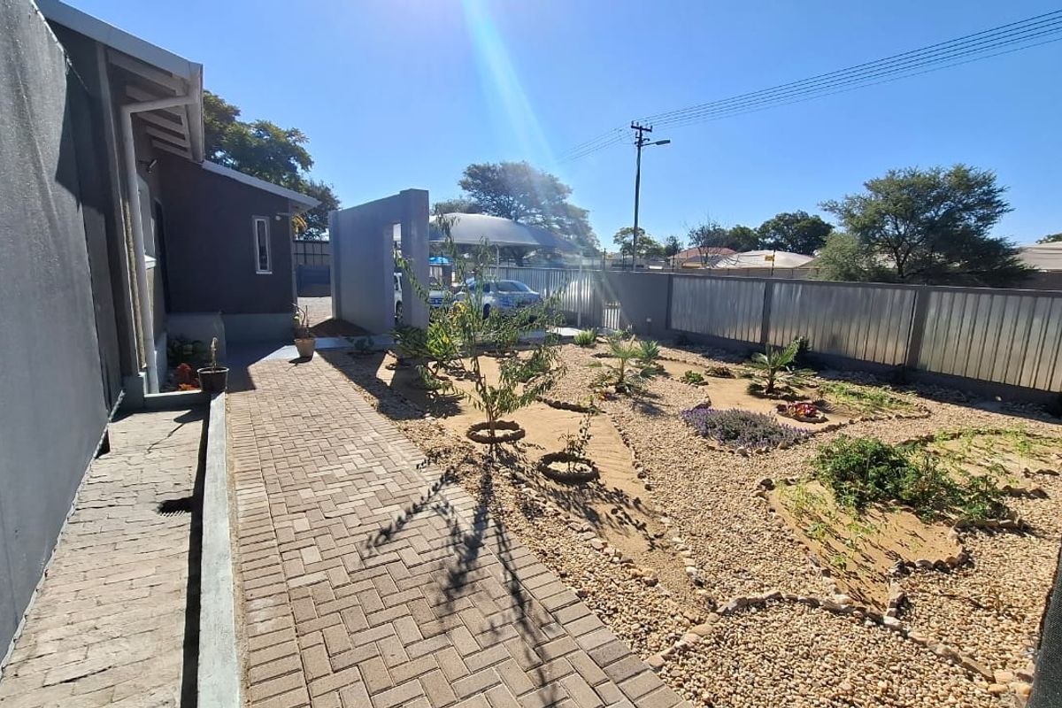 A well-maintained rear exterior area featuring a paved walkway, gravel landscaping, and secure metal perimeter fencing.