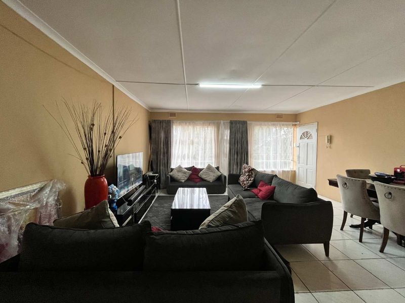 Spacious open-plan living and dining area featuring tiled flooring, neutral wall tones, and natural light through large windows with security gate access.