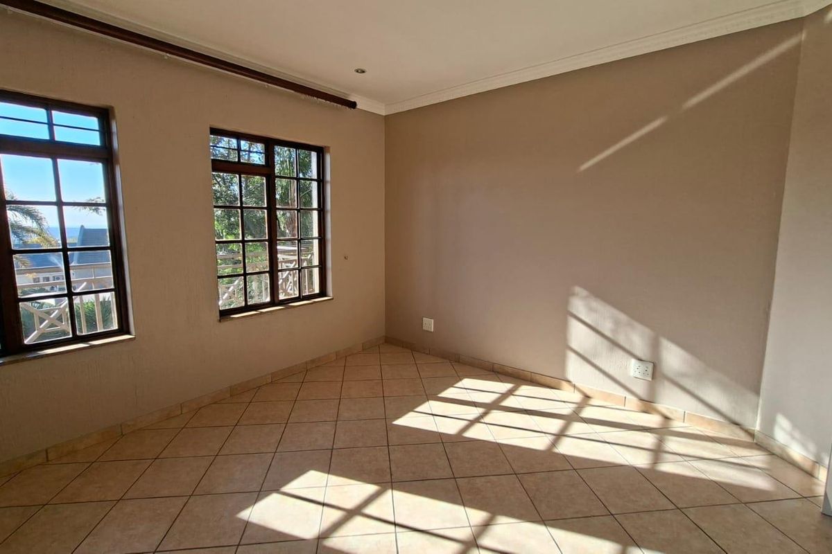 A bright and spacious bedroom featuring neutral wall tones, tiled flooring, built-in cupboards, and large windows allowing for ample natural light.