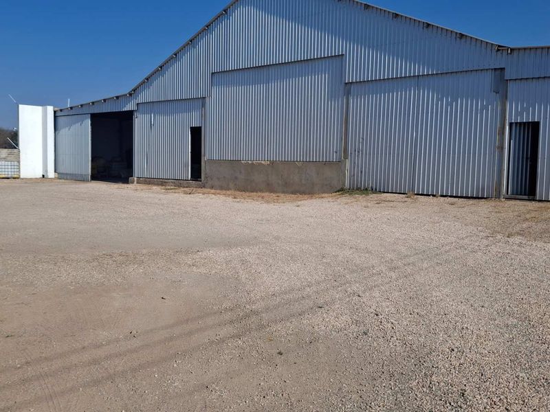 Industrial warehouse facility featuring corrugated metal cladding, large sliding access doors, and a spacious gravel yard area.