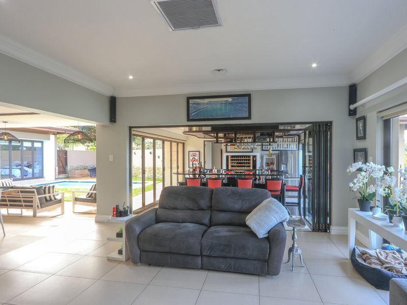 Spacious open-plan living area featuring tiled floors, recessed lighting, and seamless flow to the outdoor patio and built-in bar area through stacking glass doors.