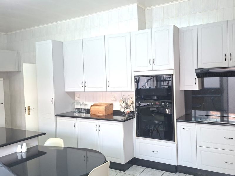 A well-maintained kitchen featuring white cabinetry, black granite countertops, built-in oven, extractor fan, and tiled finishes.