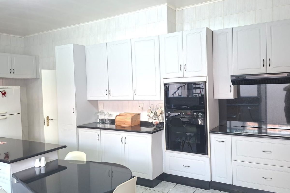 A well-maintained kitchen featuring white cabinetry, black granite countertops, built-in oven, extractor fan, and tiled finishes.