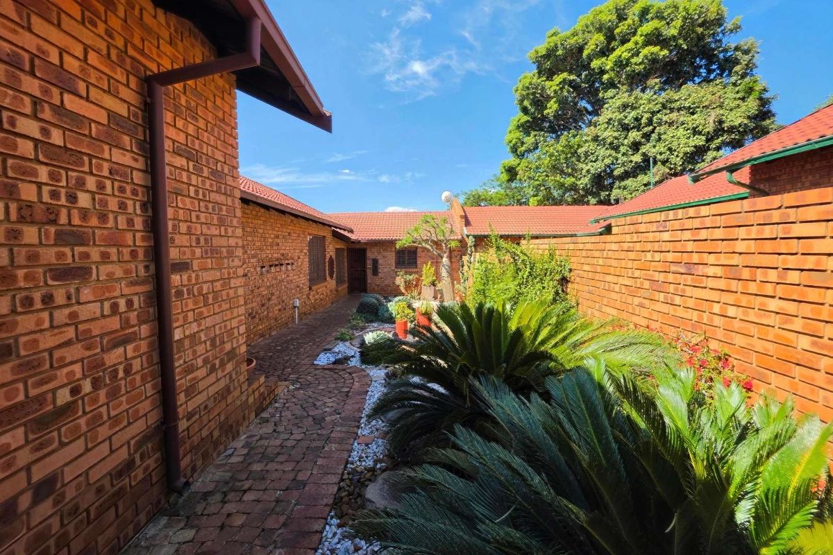 A well-maintained rear courtyard featuring face brick walls, a tiled roof, and a brick-paved pathway surrounded by established garden landscaping.