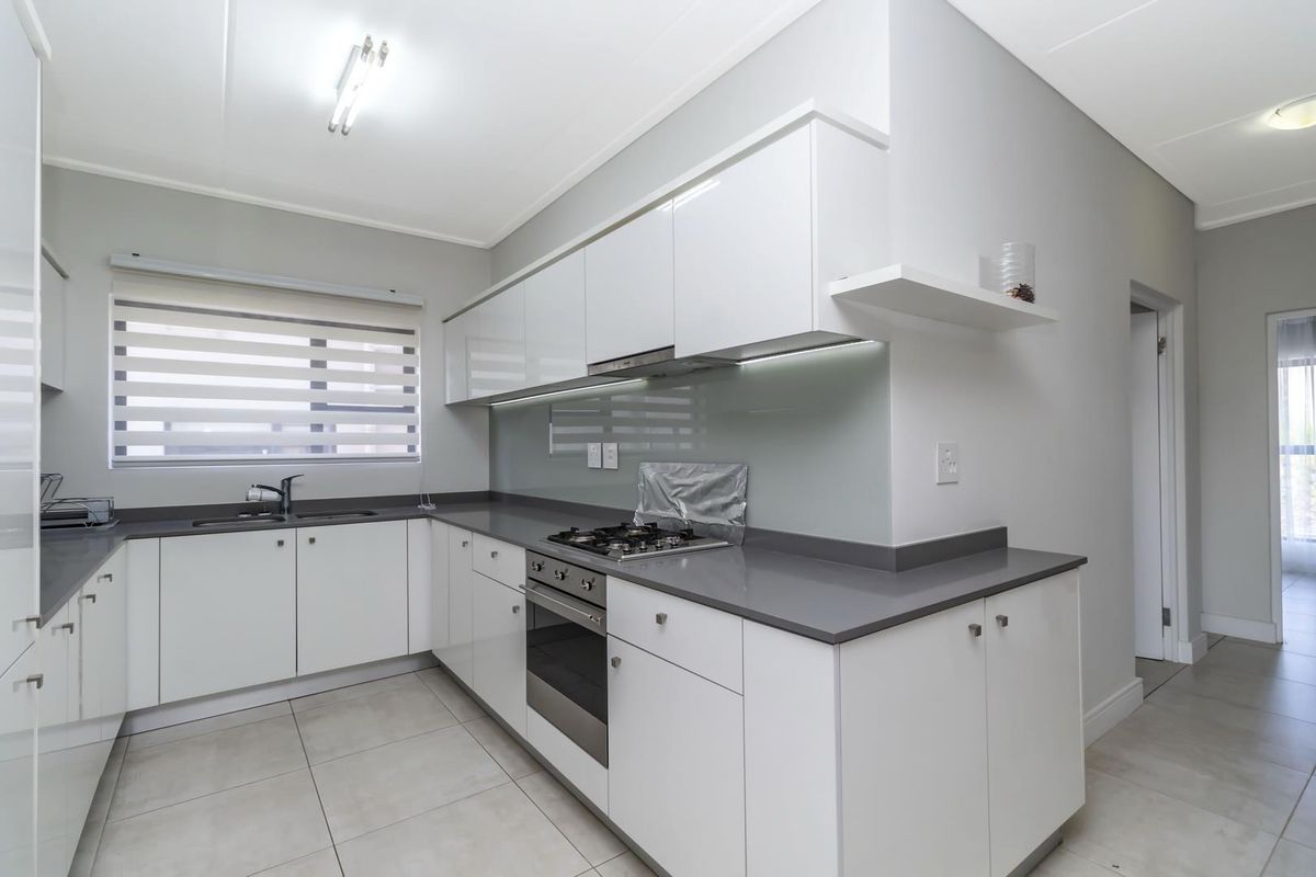 Modern kitchen featuring white cabinetry, grey stone countertops, a built-in gas hob, oven, and extractor fan with tiled flooring.