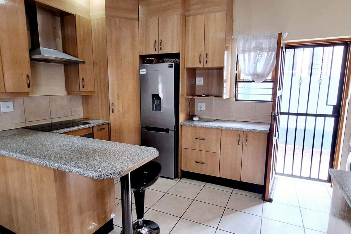 A functional kitchen featuring light wood cabinetry, granite-look countertops, a breakfast bar, stainless steel extractor fan, and direct access to an exterior door.