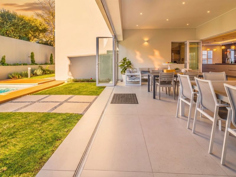 A modern covered patio featuring large format floor tiles and seamless stacking doors, overlooking a landscaped garden and swimming pool area.