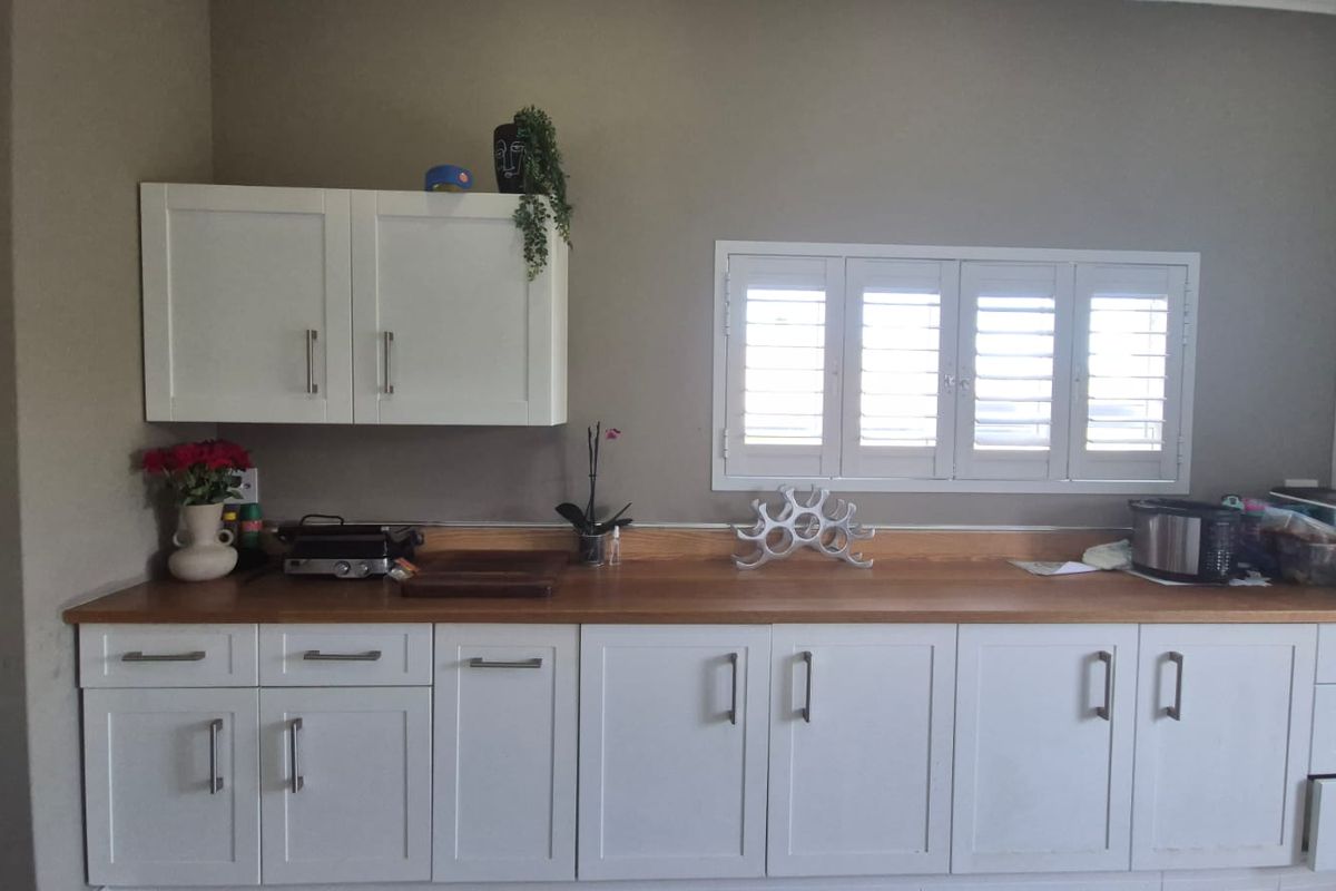 A functional kitchen area featuring white cabinetry, a wooden countertop, and plantation-style window shutters.