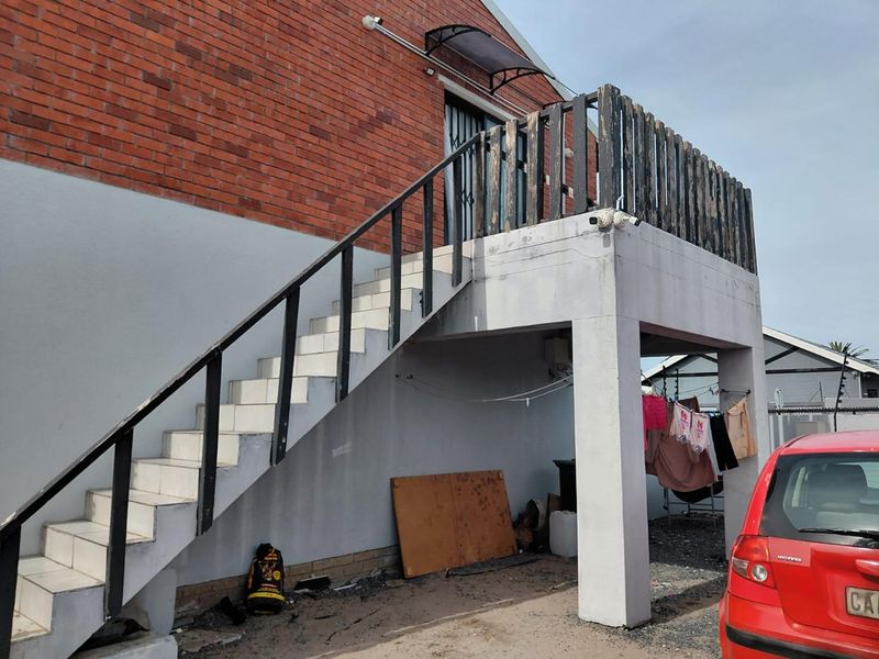 Exterior view of a brick house featuring an external staircase leading to an upper balcony with weathered timber railings.