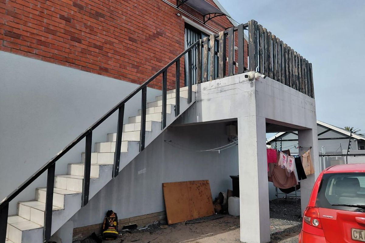 Exterior view of a brick house featuring an external staircase leading to an upper balcony with weathered timber railings.