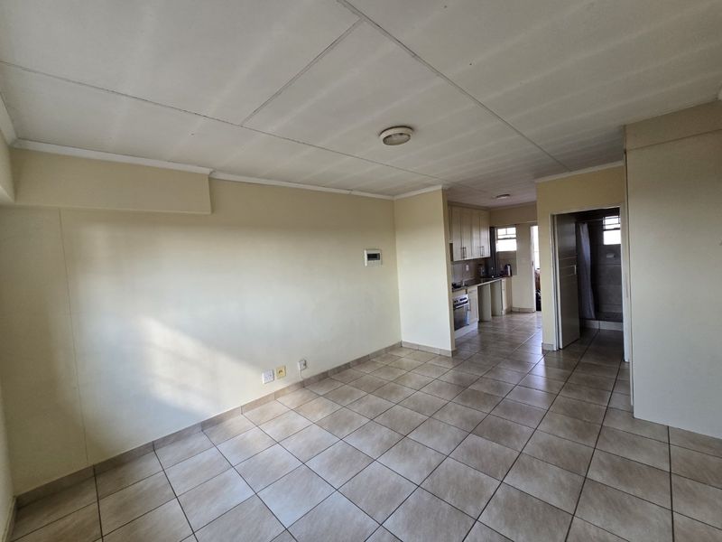 An open-plan living and kitchen area featuring tiled flooring, built-in cabinetry, and an integrated oven, offering a blank canvas for renovation.