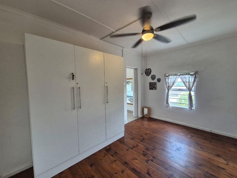 A bright bedroom featuring polished timber flooring, a built-in wardrobe, and a ceiling fan, offering a clean and functional space.