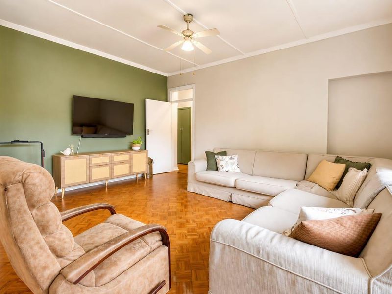 A well-maintained living room featuring classic parquet flooring, a ceiling fan, and a feature wall, offering a comfortable and inviting living space.