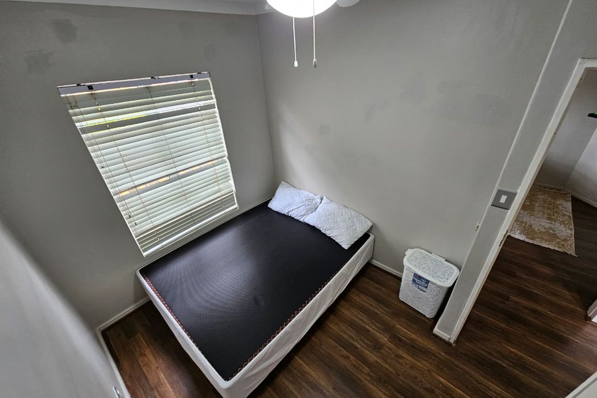 A compact bedroom featuring dark wood-look flooring, a ceiling fan with integrated light, and a window fitted with horizontal blinds.