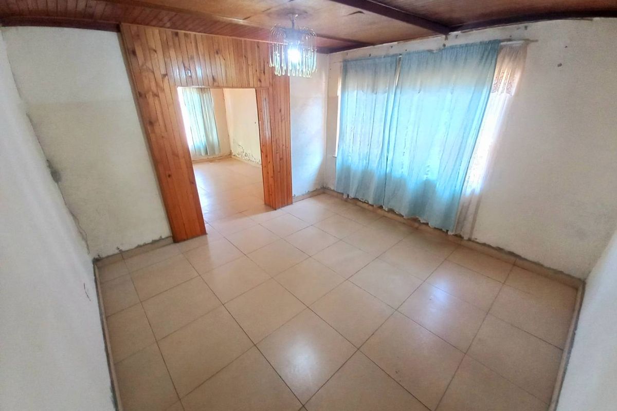 An empty living room featuring tiled flooring, a timber-paneled ceiling, and a wooden door frame leading to an adjacent room.