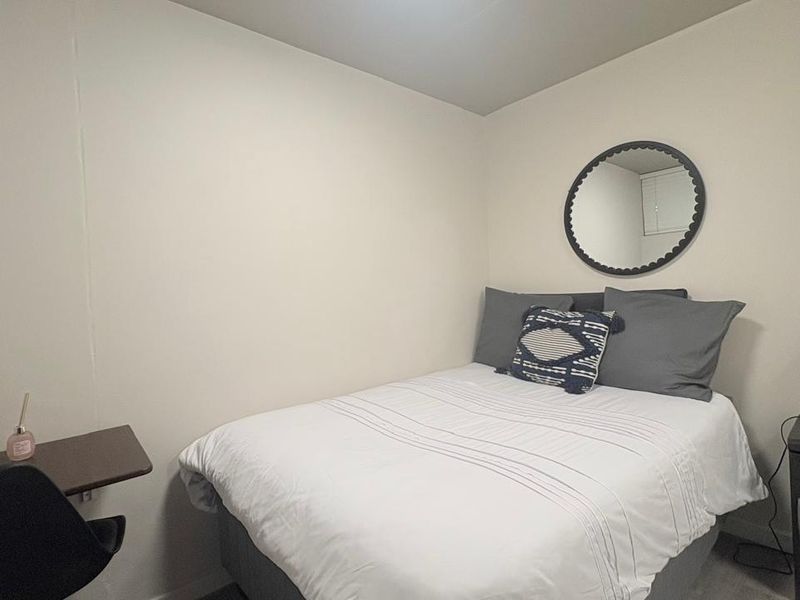 A compact bedroom featuring neutral wall finishes and a functional layout suitable for a single bed and workspace.