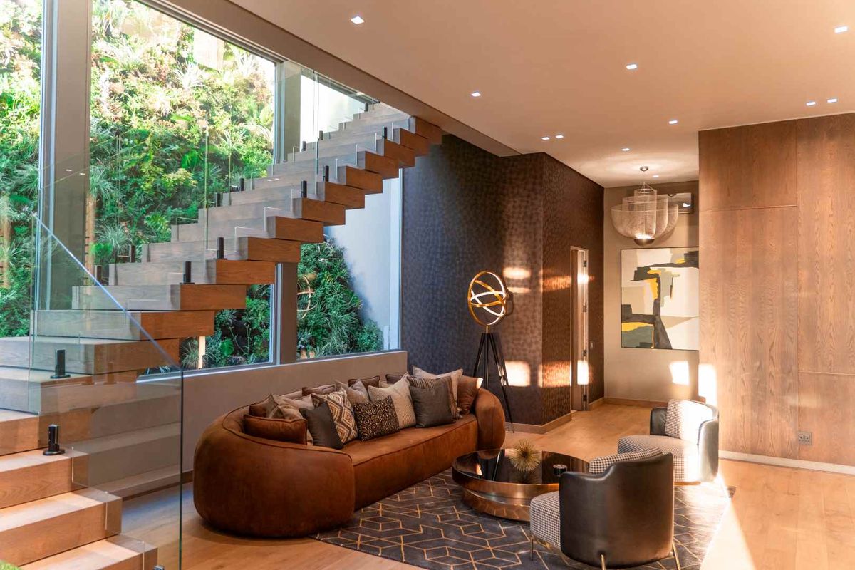 Modern living area featuring a striking floating timber staircase, floor-to-ceiling glass windows, and high-end finishes with a view of a lush vertical garden.
