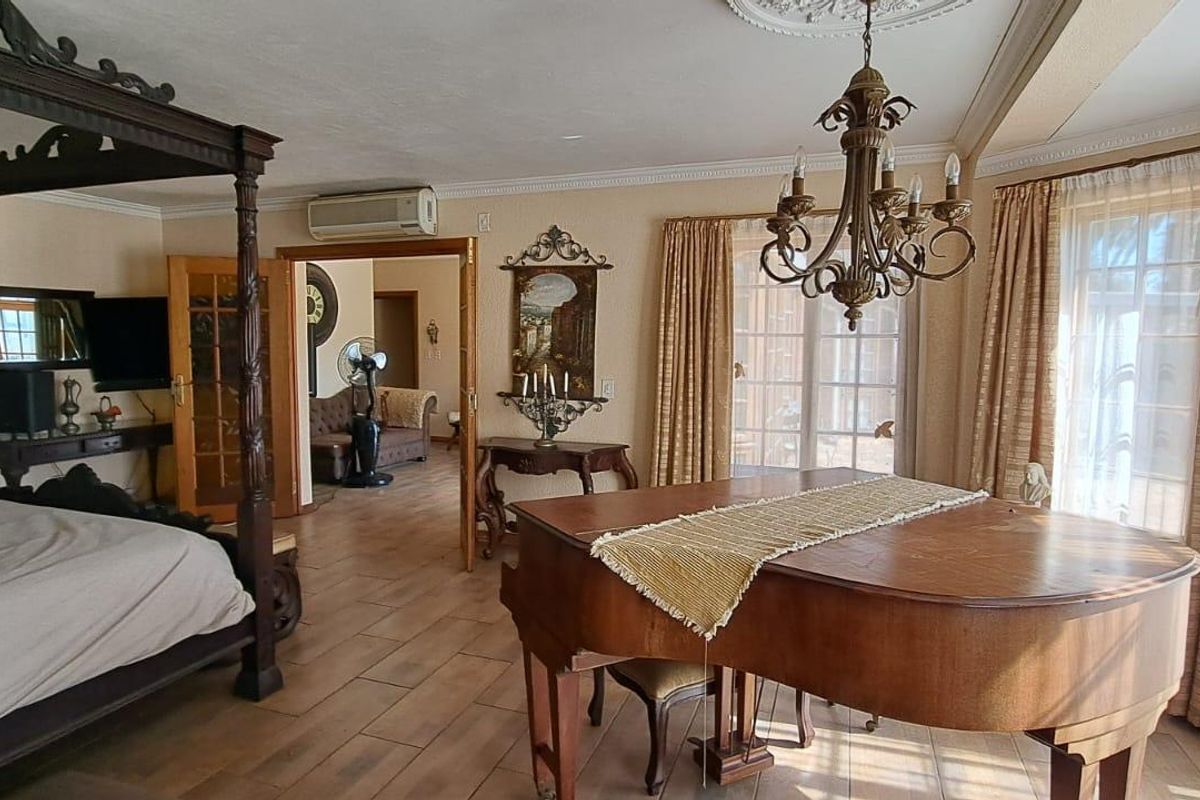 Spacious bedroom featuring tiled flooring, decorative ceiling rose with chandelier, and direct access to an adjoining living area.