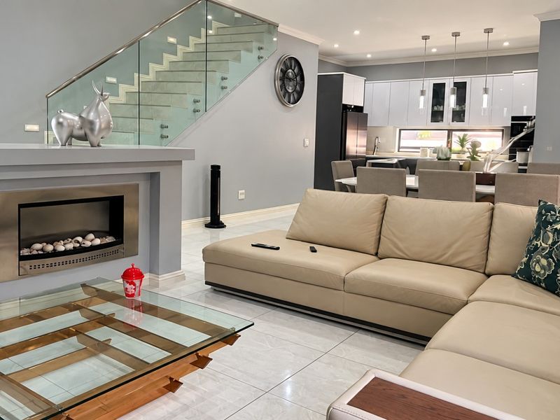 Spacious open-plan living area featuring a modern built-in fireplace, glass staircase balustrade, and a contemporary kitchen with sleek cabinetry and island seating.