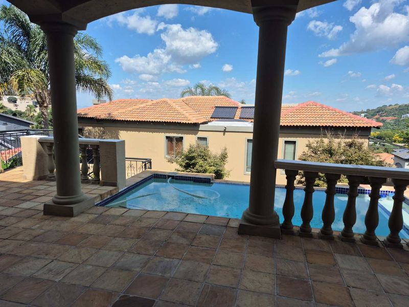 Covered patio featuring stone columns and balustrades, overlooking a private swimming pool with solar heating panels and views of the surrounding estate.