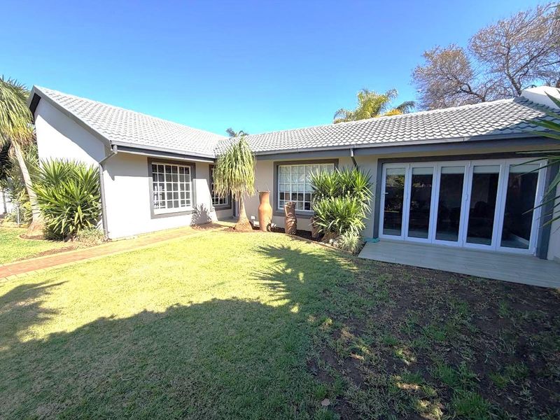 Rear view of the house featuring a well-maintained lawn, paved walkway, and modern sliding glass doors leading into the living area.