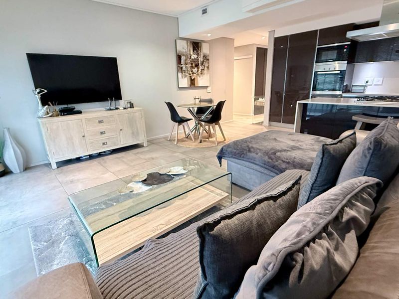 Modern open-plan living area featuring a sleek kitchen with integrated appliances, stone countertops, and tiled flooring, seamlessly flowing into the lounge space.