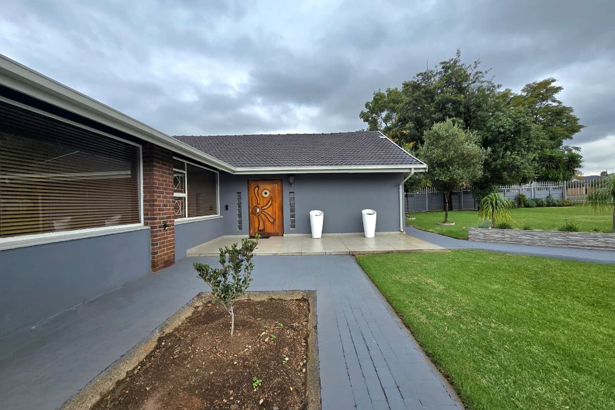 A well-maintained rear exterior view featuring a paved patio area, landscaped lawn, and a modern entrance door with decorative detailing.