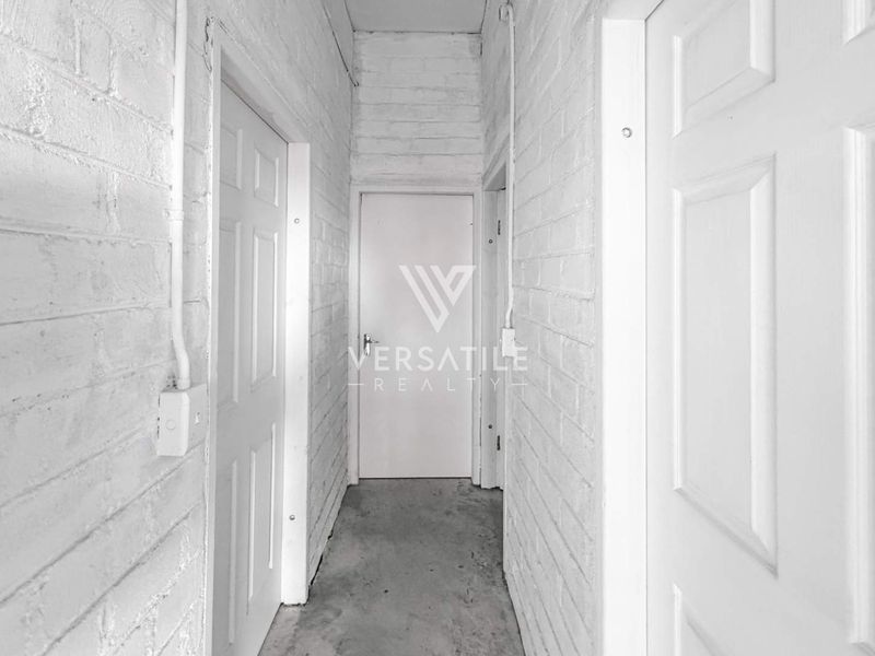 A narrow industrial-style hallway featuring painted exposed brick walls, surface-mounted electrical conduits, and multiple internal doors.