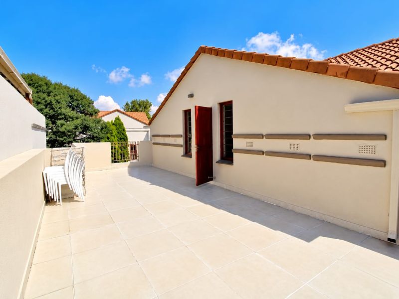 A spacious, well-maintained open-air balcony featuring light-colored floor tiles, terracotta roof detailing, and direct access to the interior.