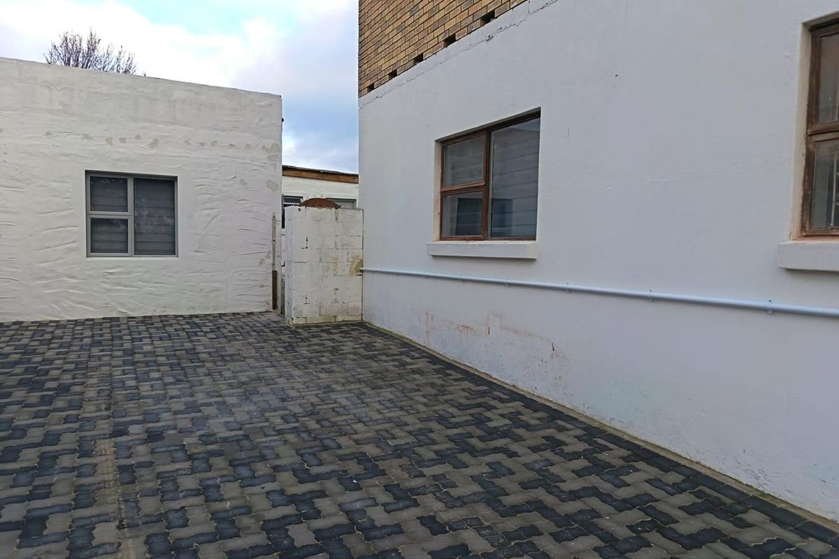 A paved rear courtyard area featuring white rendered walls, brick detailing, and aluminium-framed windows, providing a functional outdoor space.