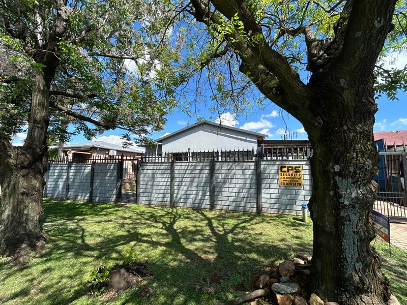 Front view of the property featuring a secure precast concrete boundary wall with metal spikes, mature trees, and a well-maintained lawn.