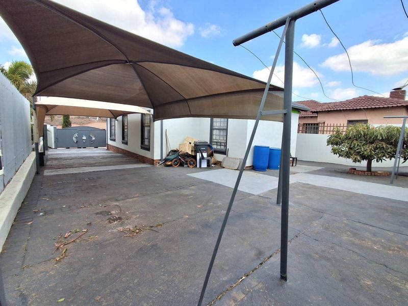 Rear exterior area featuring a paved driveway, shade sail structure, and perimeter boundary walls.