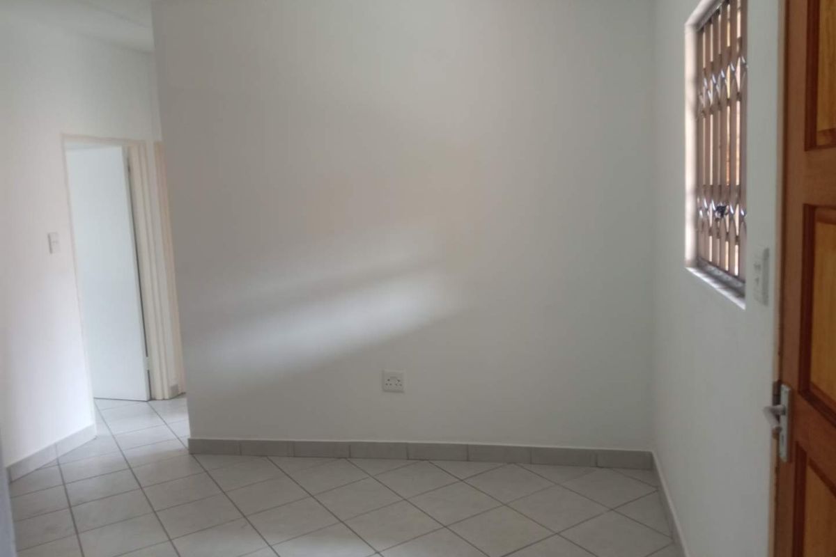 A bright, empty room featuring neutral tiled flooring, white walls, and a window fitted with a security gate.