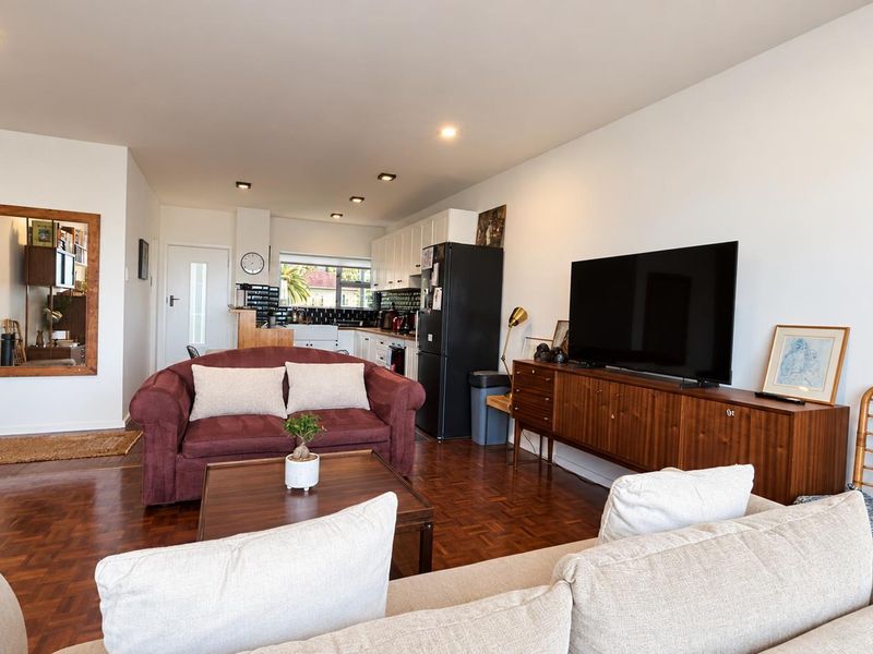 An open-plan living and kitchen area featuring warm parquet flooring, recessed lighting, and a functional kitchen layout with tiled backsplash.