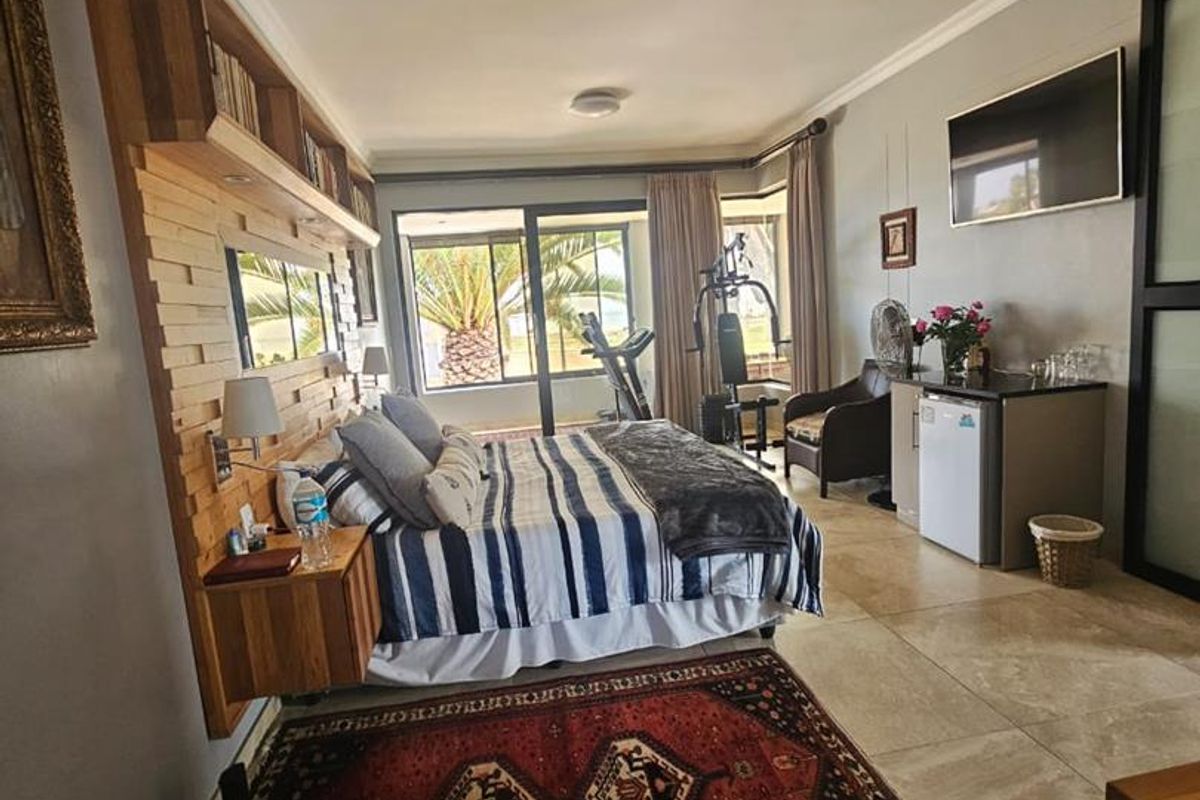 Spacious bedroom featuring tiled flooring, a custom timber headboard with integrated shelving, and large sliding glass doors leading to an outdoor area.