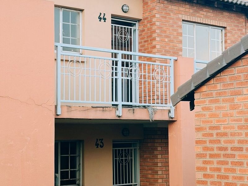 Exterior view of a two-story apartment building featuring brick and plastered facades, a balcony with a security gate, and tiled roofing.