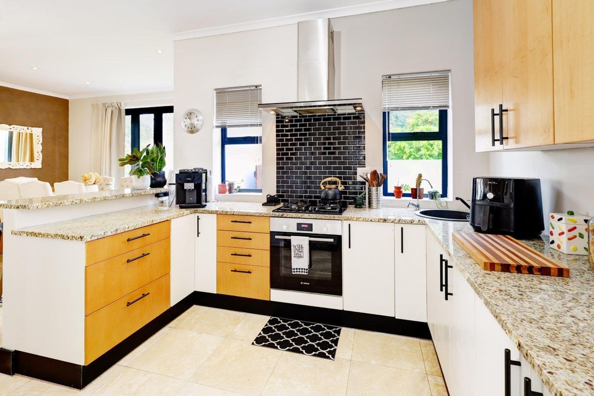 Modern kitchen featuring granite countertops, a built-in oven with gas hob, stainless steel extractor fan, and a mix of light wood and white cabinetry.