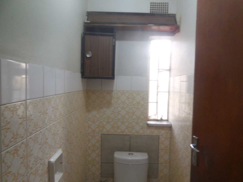 A compact bathroom featuring dated wall tiles, a wall-mounted storage cabinet, and a window for natural light.