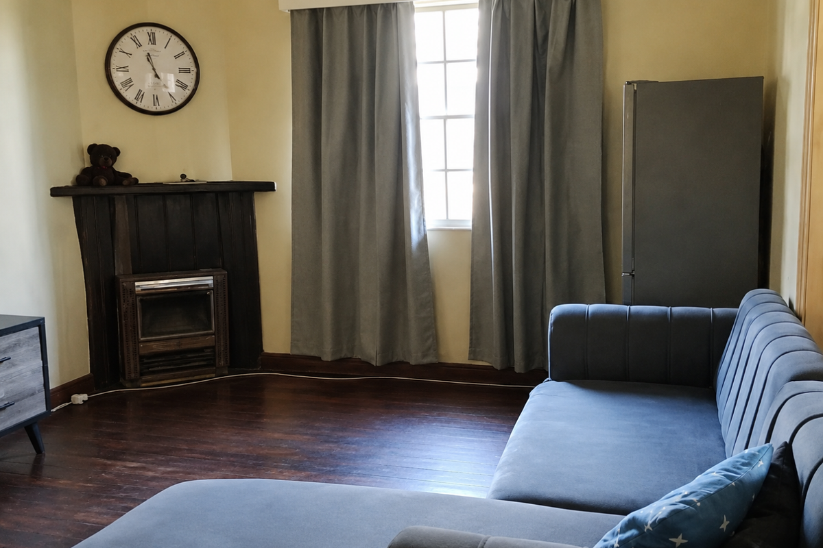 A living room featuring dark timber flooring and a traditional fireplace, offering a cozy atmosphere with natural light from the central window.