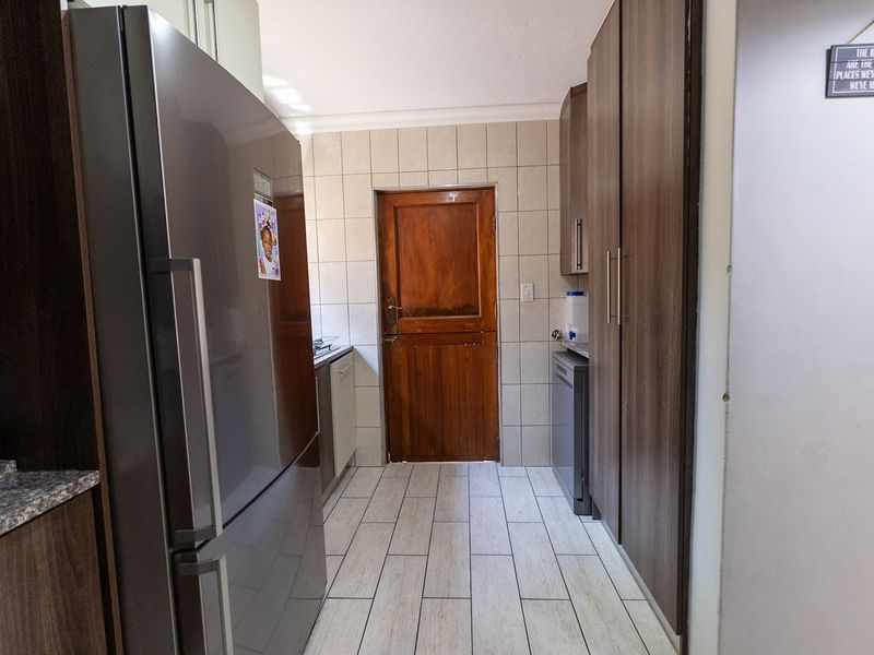 A functional scullery area featuring built-in cabinetry, granite countertops, tiled flooring, and a solid wood door leading to the exterior.