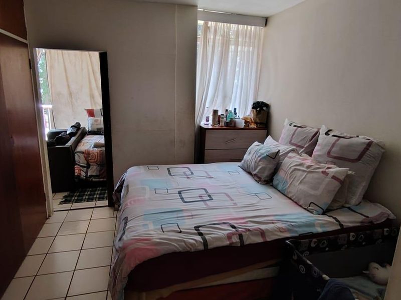 A bedroom featuring built-in cupboards and tiled flooring, with visible wear on the wall surfaces requiring maintenance or repainting.