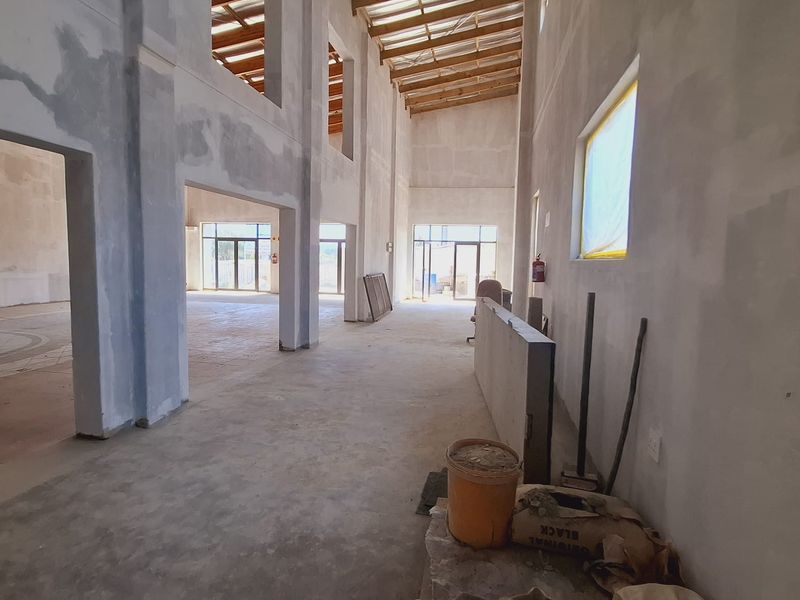 Spacious open-plan interior under construction, featuring double-height ceilings with exposed timber trusses and concrete flooring, offering a blank canvas for custom finishes.